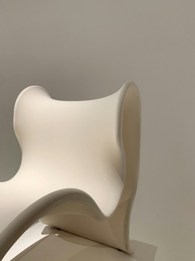 Scaun alb sculptural, cu forme curbe, în lumină laterală blândă