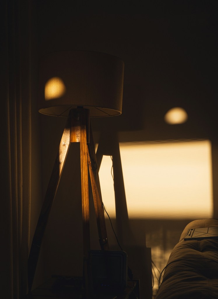 Lampadar cu picioare de lemn și abajur textil în lumina caldă a serii