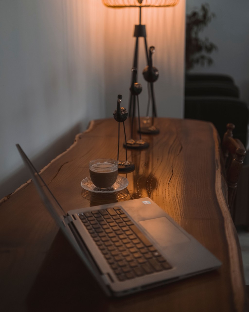 Masă din lemn masiv cu laptop și o ceașcă de cafea, în lumina caldă a unei lămpi de seară
