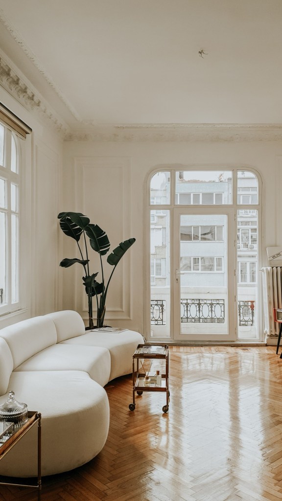 Apartament vechi cu stucaturi și parchet în os de pește, mobilat cu o canapea albă curbată de azi, lângă o ușă de balcon arcuită