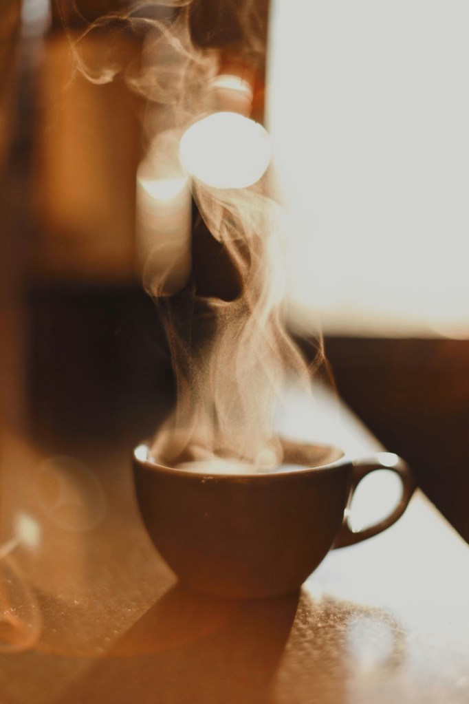 Ceașcă de cafea aburindă în lumina dimineții, lângă fereastră
